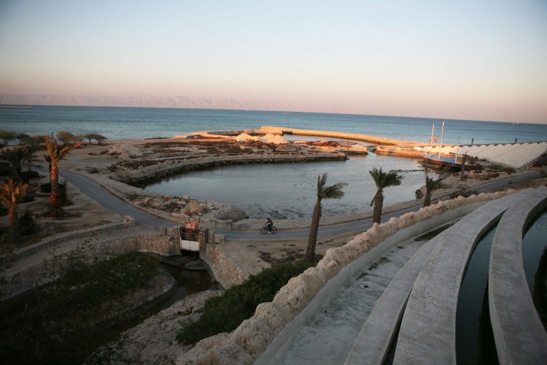 Artificial lakes with rusting ship and palm trees on Kish island beach at sunset.