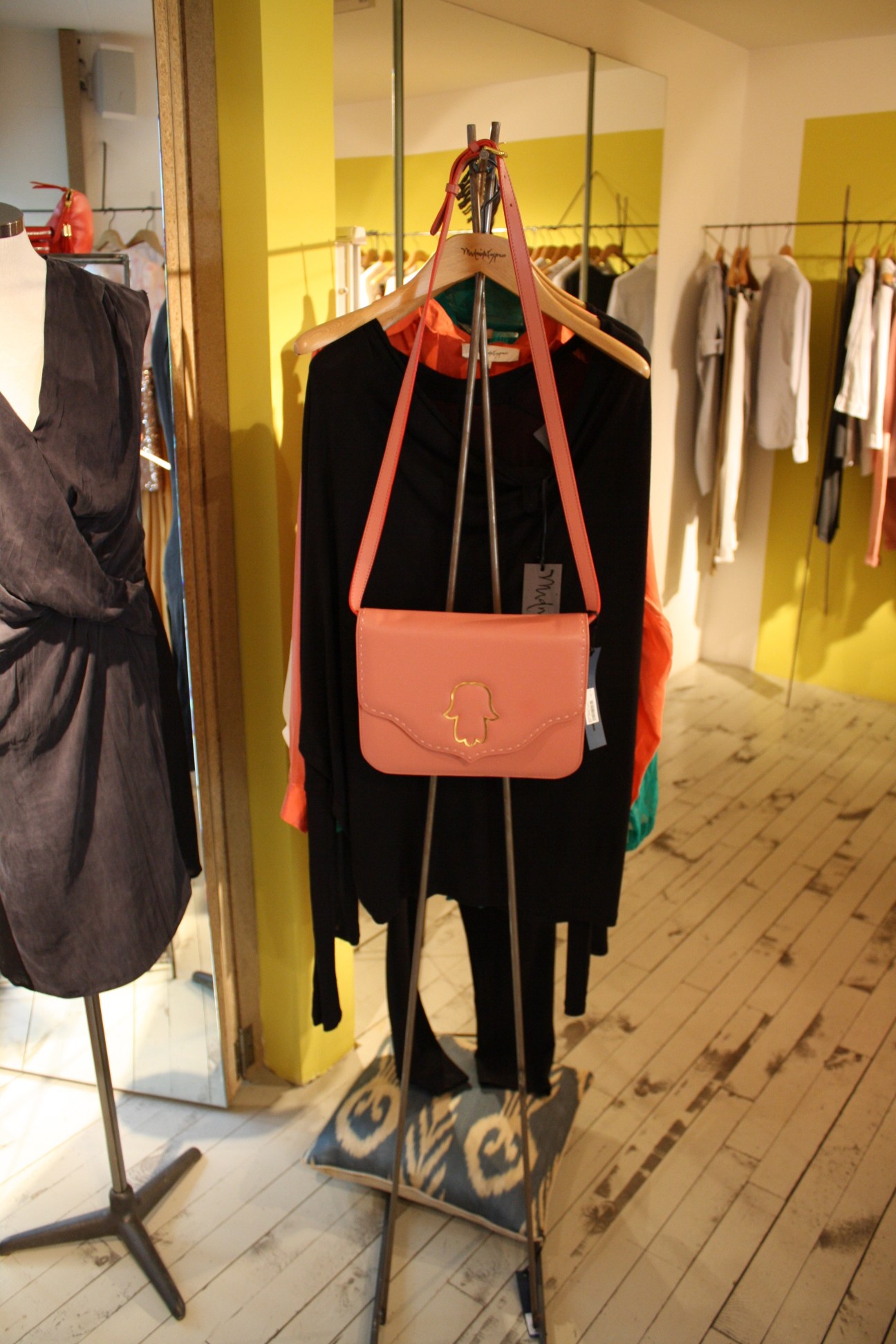 Mannequin displaying black cardigan with red trim and coral shoulder bag with hamsa hand emblem in fashion boutique.