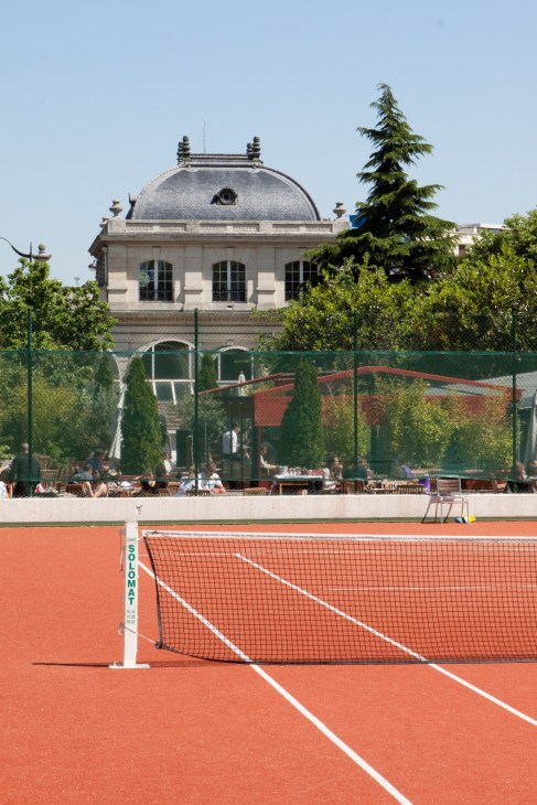 Clay tennis court with net at a historic Paris tennis club building with dome roof