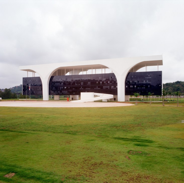 Oscar Niemeyer's Administrative City building with curved white roof and dark panel sections on green lawn.