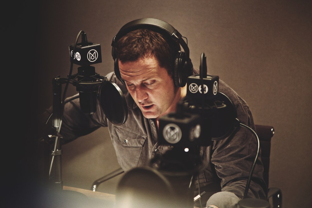 Voiceover artist Joel Beckett recording in a studio with microphone and headphones.