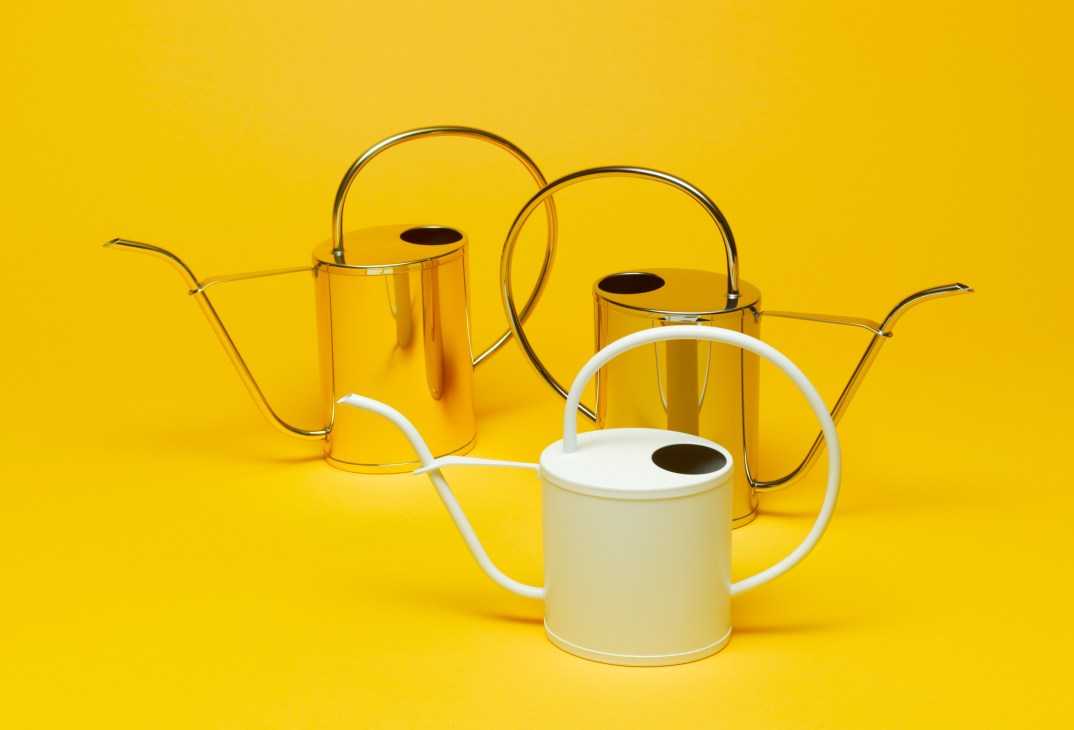 Three Hogri watering cans in yellow, yellow, and white with curved handles against a yellow background.