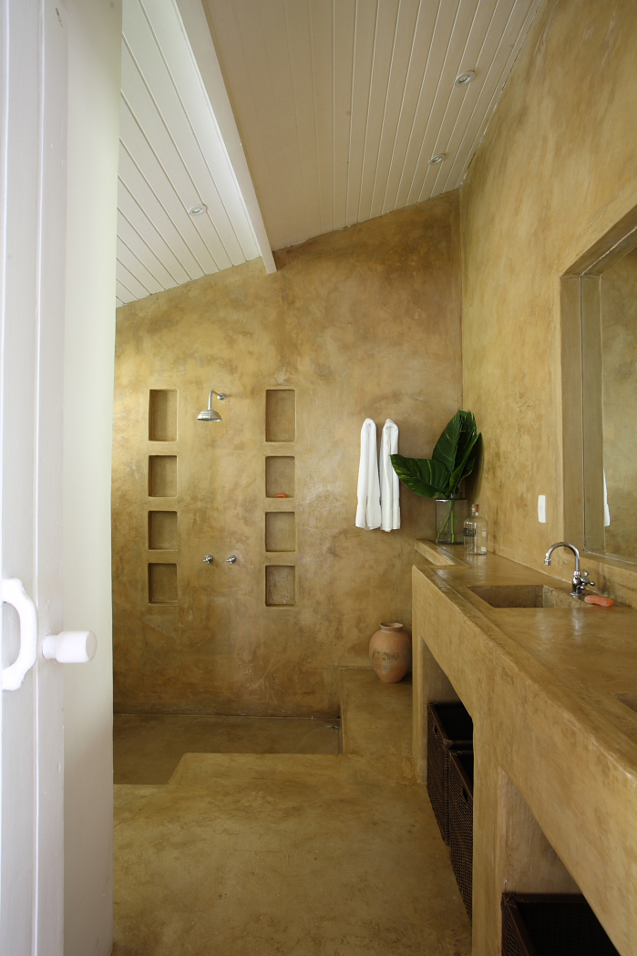 Modern bathroom with ochre plaster walls, recessed shelving, wooden sink counter, and rainfall showerhead.