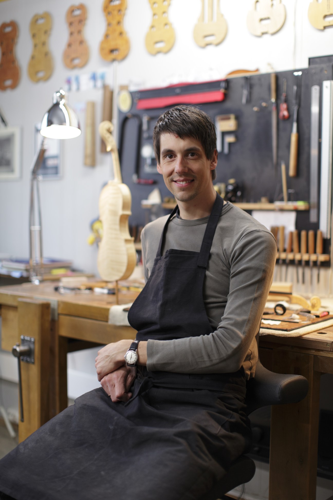 Jacob von der Lippe, a violin maker, sits in his workshop surrounded by violin parts and tools.