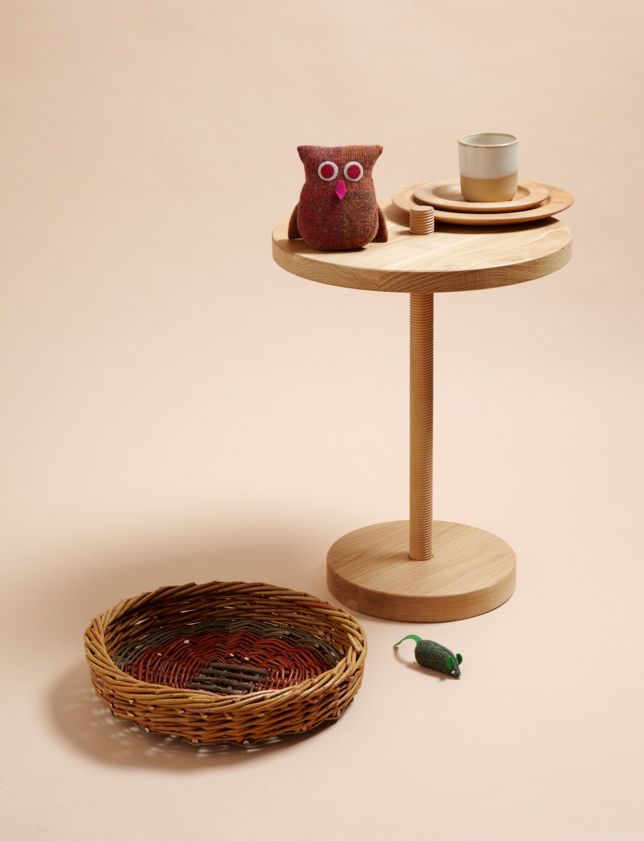 Wooden table with Irish craft items including a knitted tweed owl, earthenware mug, wooden plates, woven willow basket and small green figurine.