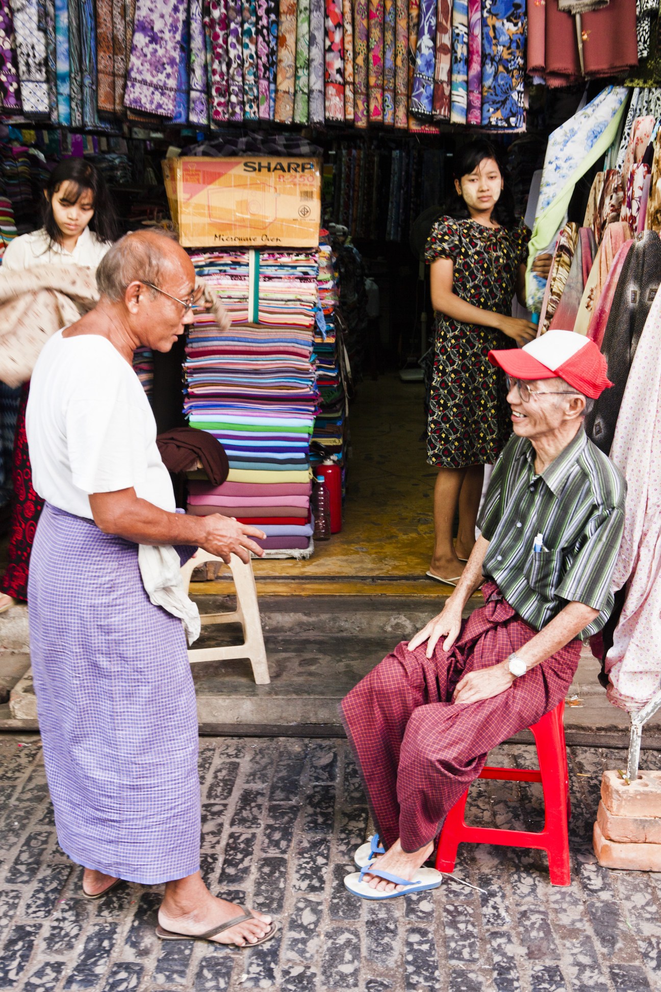Vendors and shoppers at a fabric stall in Scott Market displaying colorful textiles.