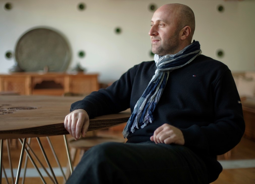 Salih Teskeredzic, a designer, sits at a wooden table in a workshop setting.