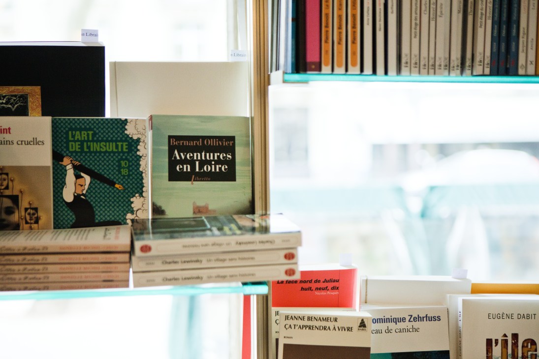 Books displayed on a turquoise shelf at Tschann Libraire bookstore in Paris, including titles by Bernard Ollivier and other French literature.