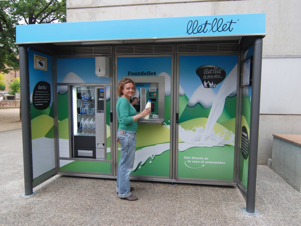 Woman using a Llet Llet milk vending machine with blue and green branding in Catalonia.
