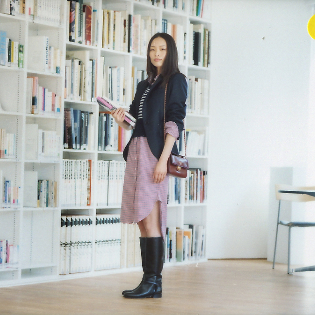 Woman in business attire posing in front of library shelves holding a pink folder.