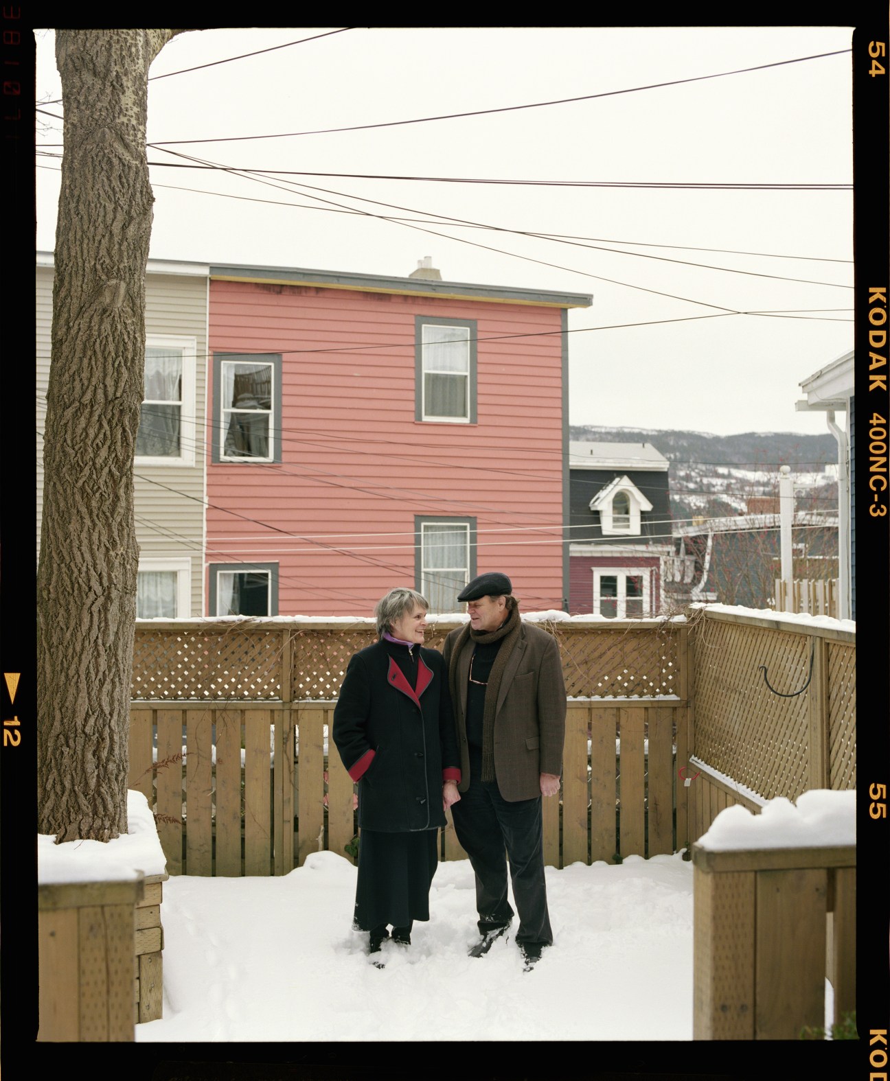 Couple standing in snow with colorful houses in background in Newfoundland