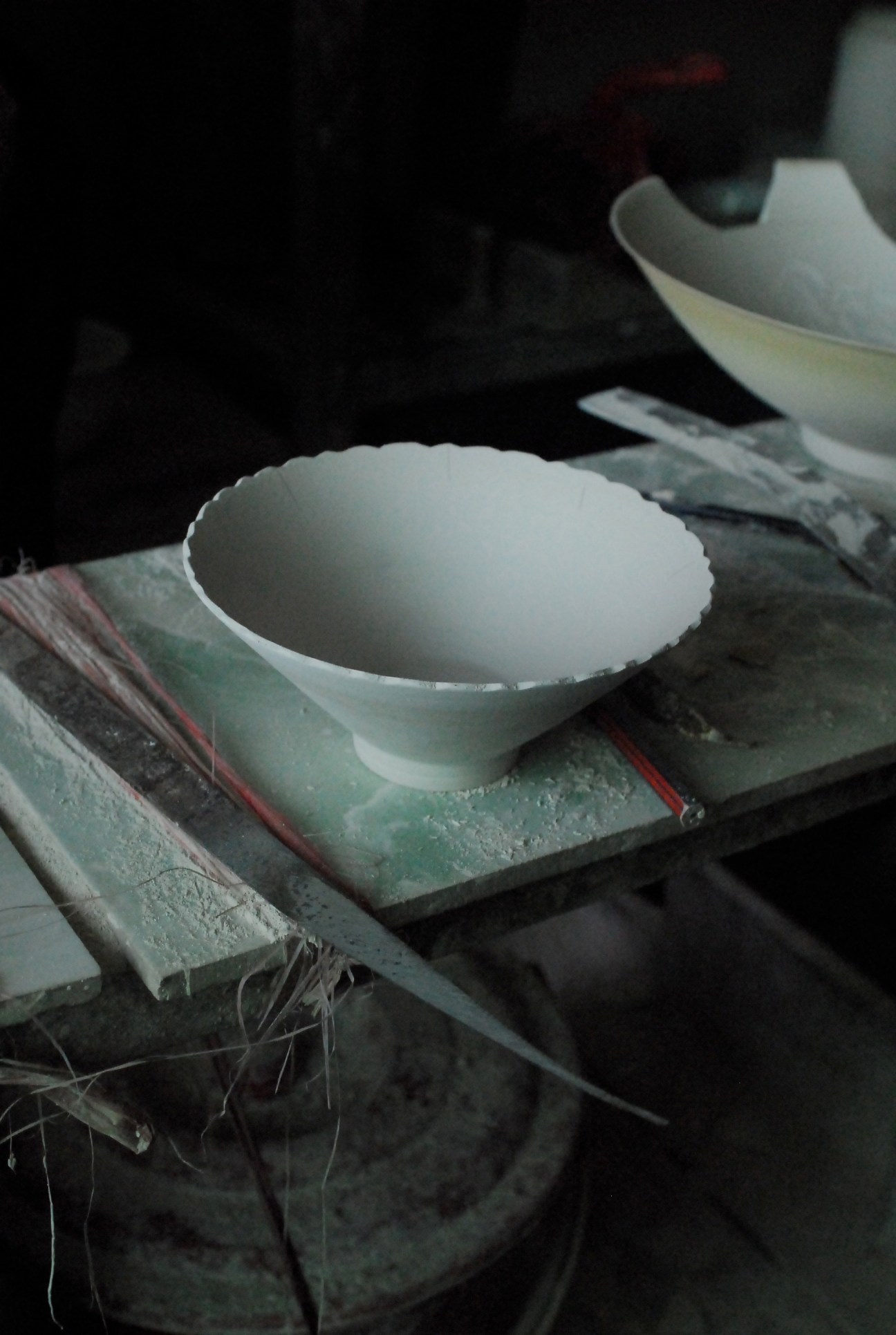 White porcelain bowl drying on a clay work surface in a pottery factory.