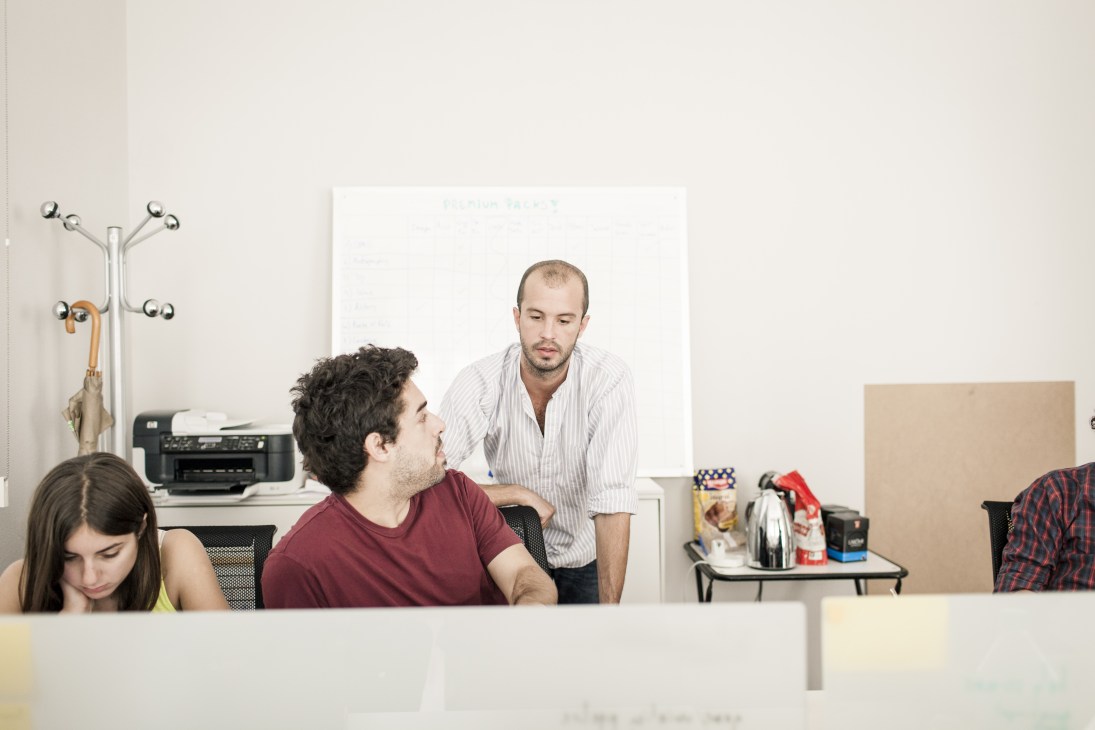 Andres Burdett, founder of uSpeak language app, stands in a modern office workspace with colleagues.