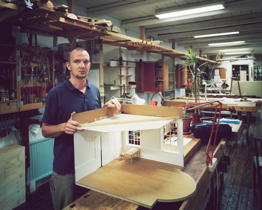 Cabinet-making student John Bøge holds a wooden furniture piece in a workshop studio.