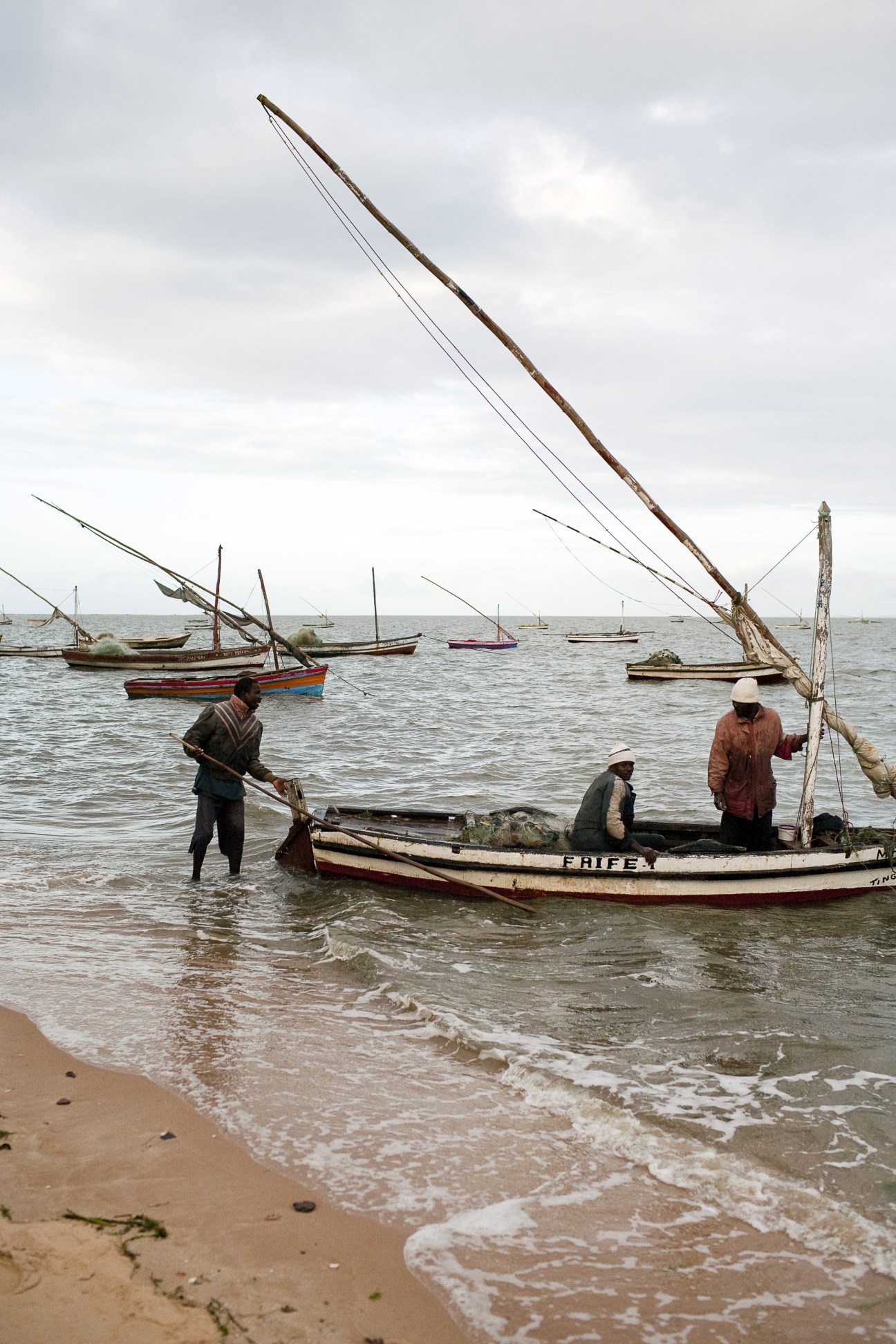 Fishermen unload their catch from a traditional wooden dhow boat in shallow waters off Maputo's beach.