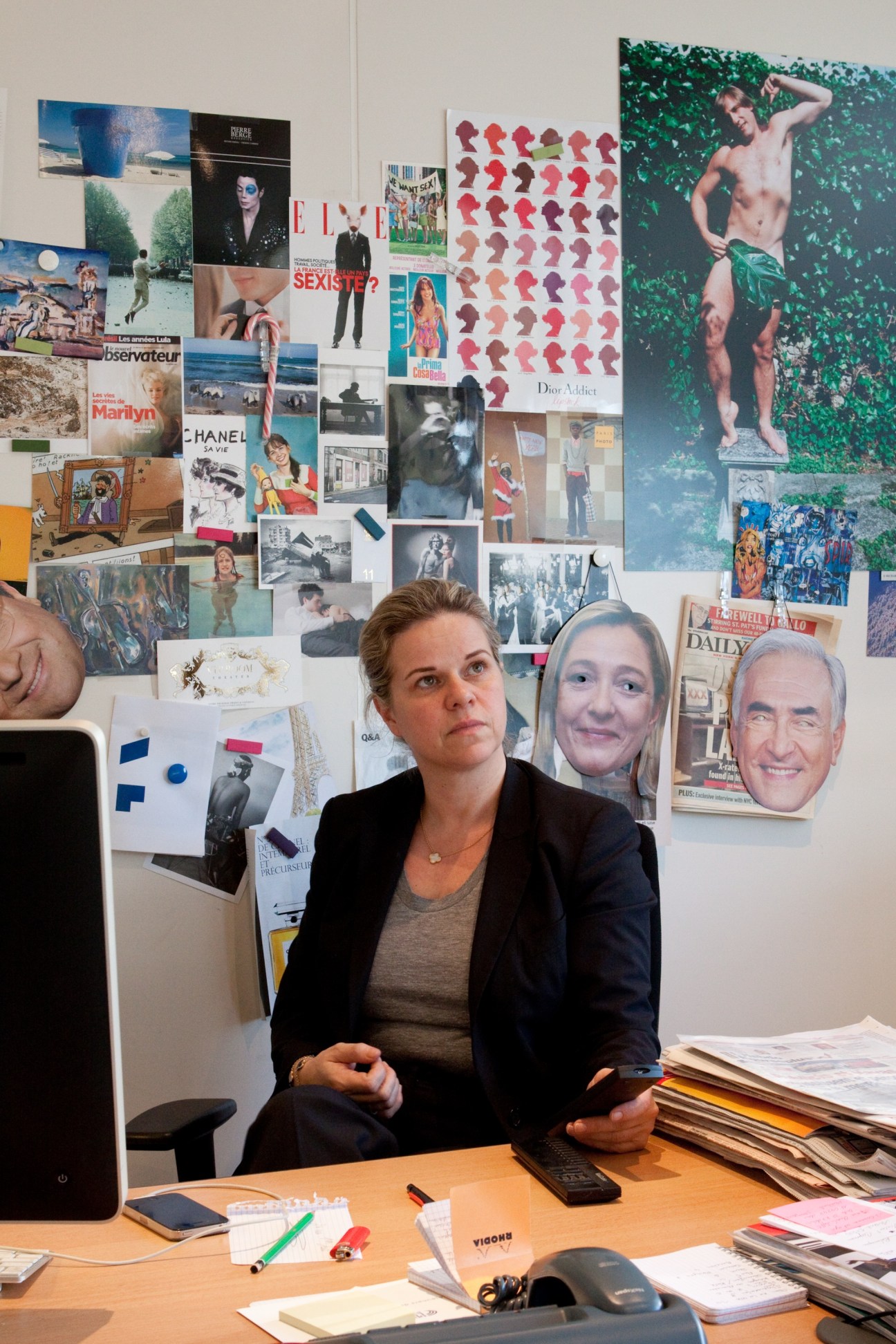 Chief news editor Caroline Mangez sitting at her desk with a collage of magazine clippings and photographs on the wall behind her.