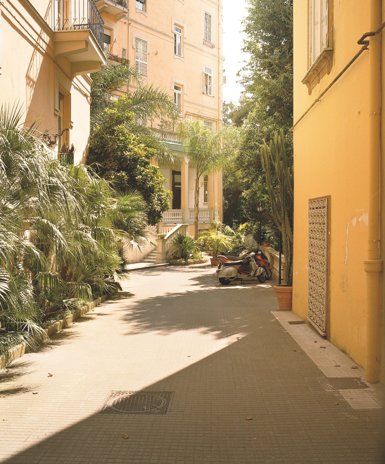 A sunlit courtyard in Vomero with yellow-ochre buildings, palm trees, and a Vespa parked against a yellow wall.