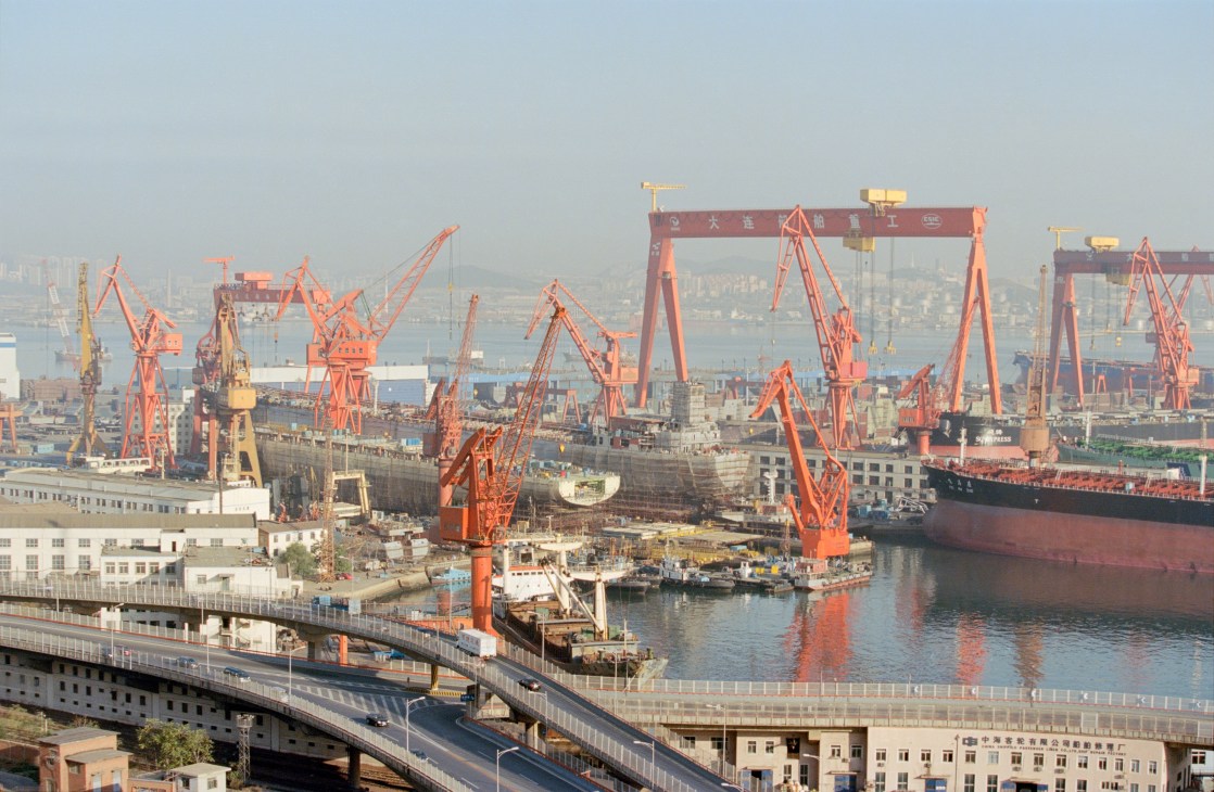 Dalian shipyard with red cranes and construction equipment along the waterfront.