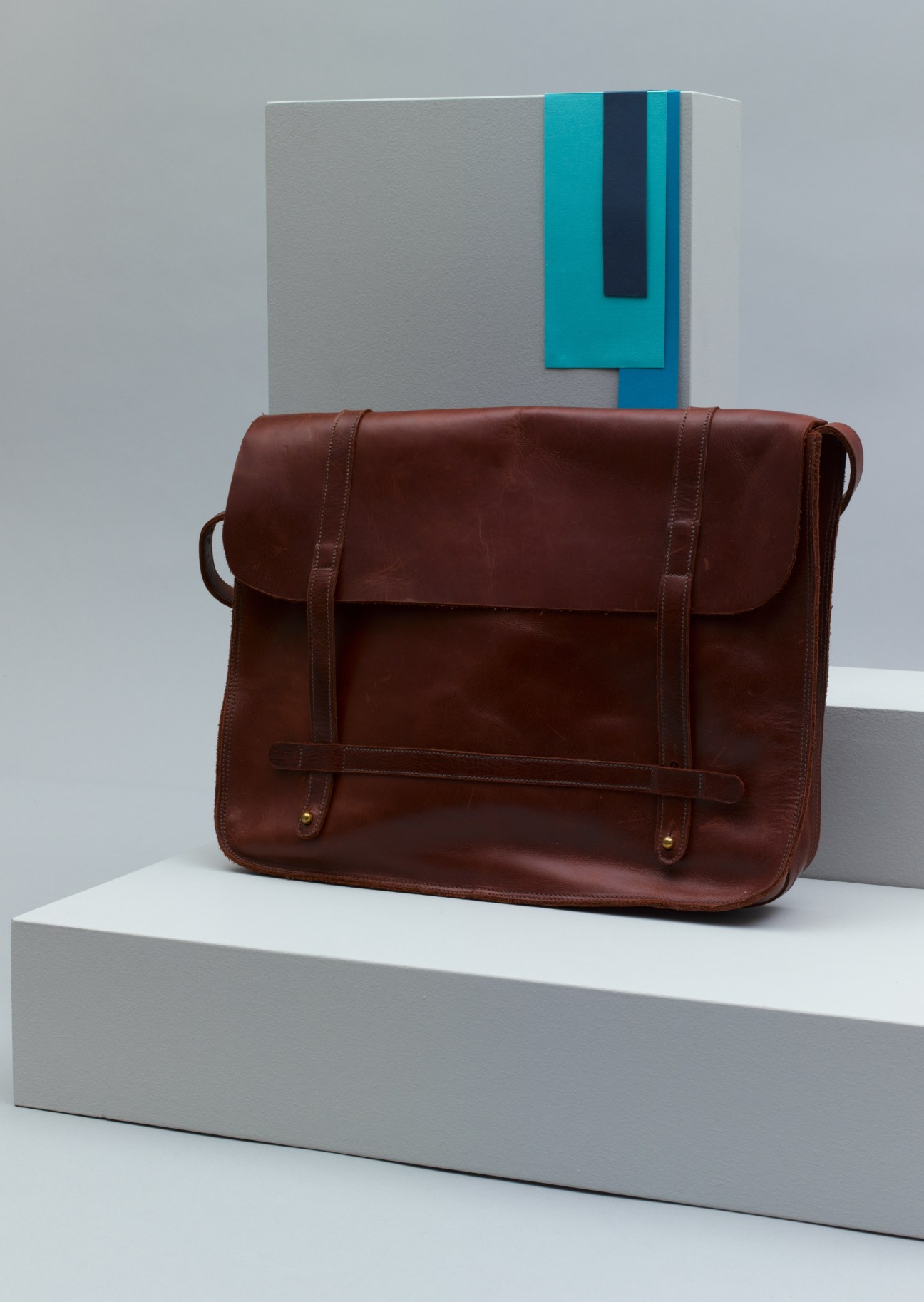 Brown leather Basil Racuk computer case with adjustable straps displayed on white platform.