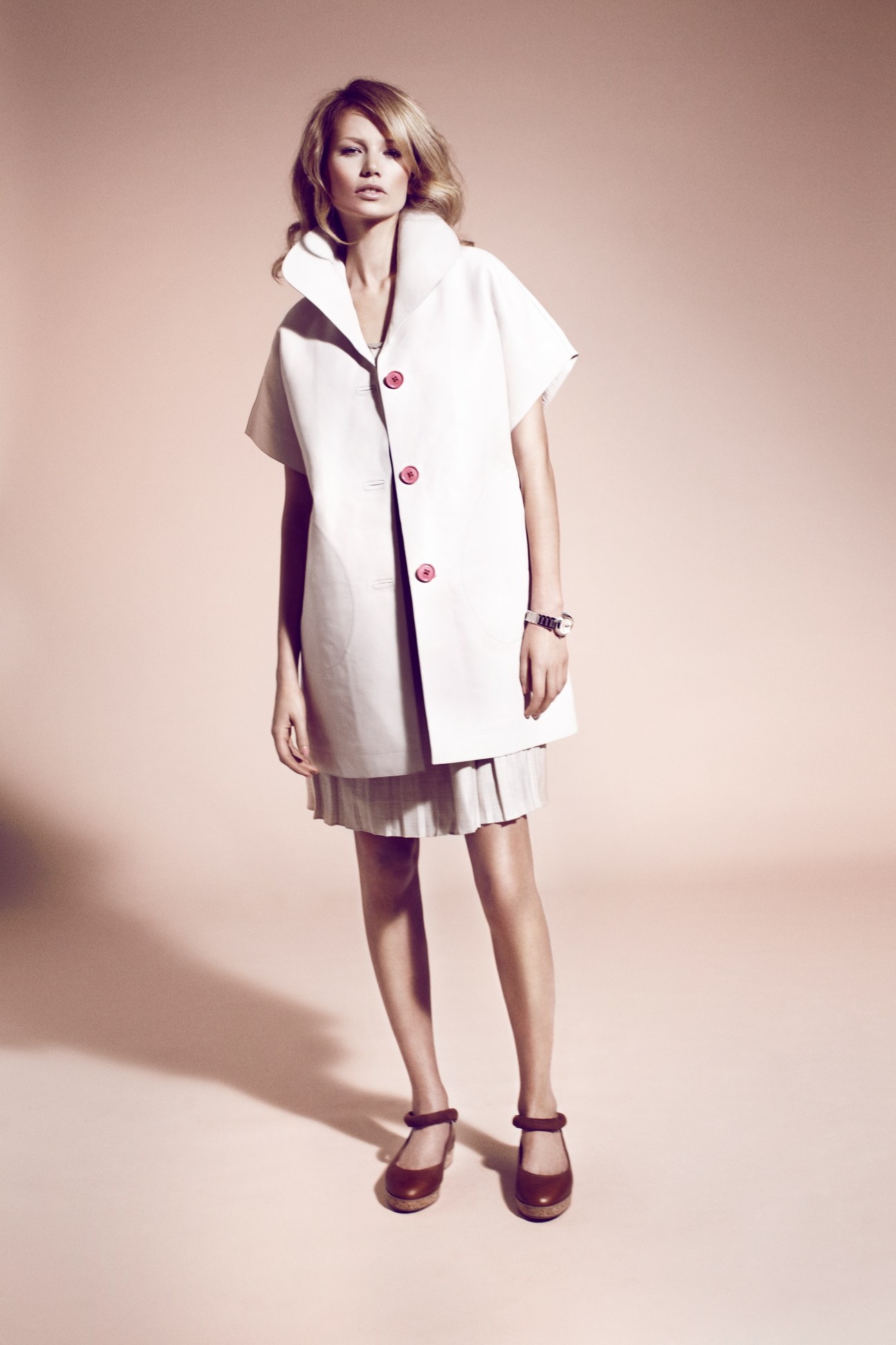 Model wearing a white Loewe coat with pink buttons over a pleated J.Crew dress and Dušan platform shoes.