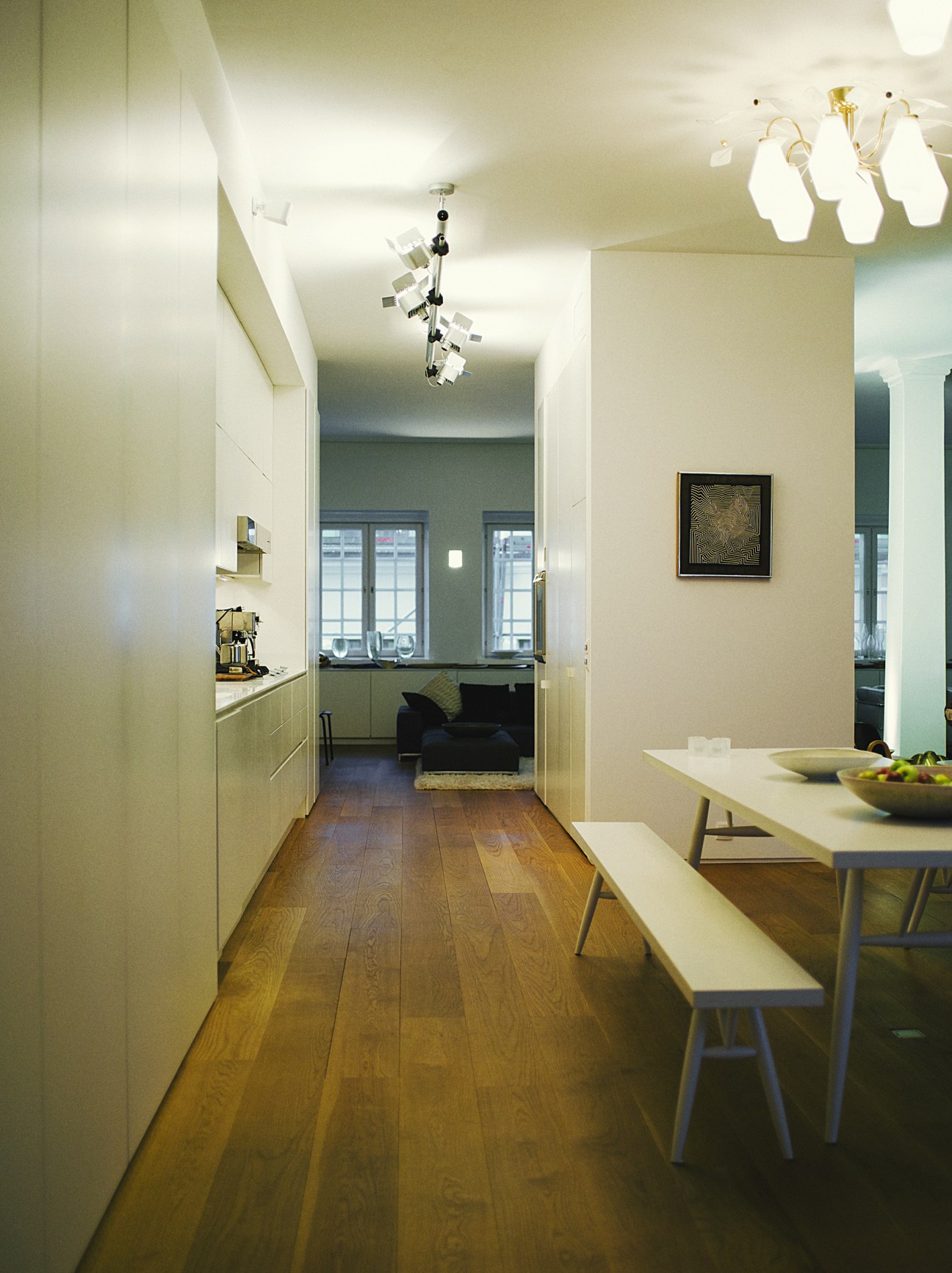 Modern kitchen with white cabinetry, wooden dining table and bench, and minimalist light fixtures.