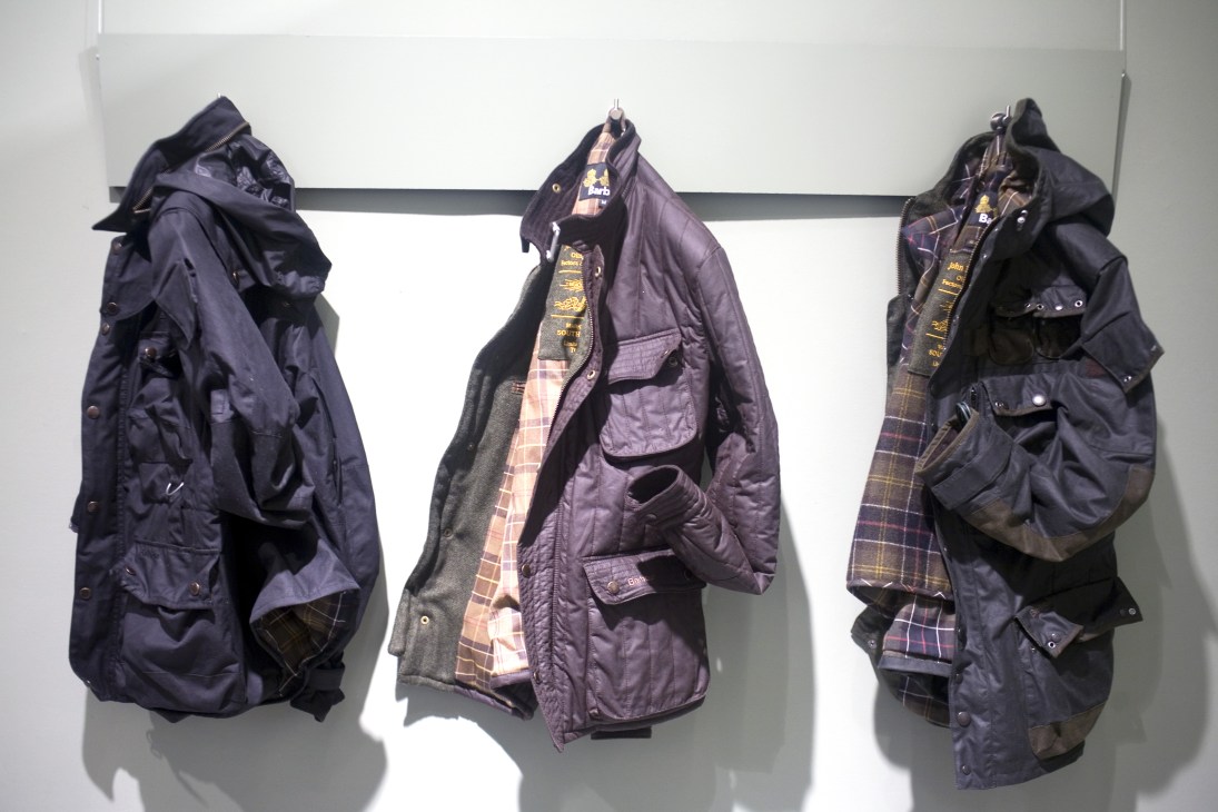 Three Barbour x To Ki To jackets displayed on hangers, featuring navy nylon shells with plaid lining in purple and red tones.