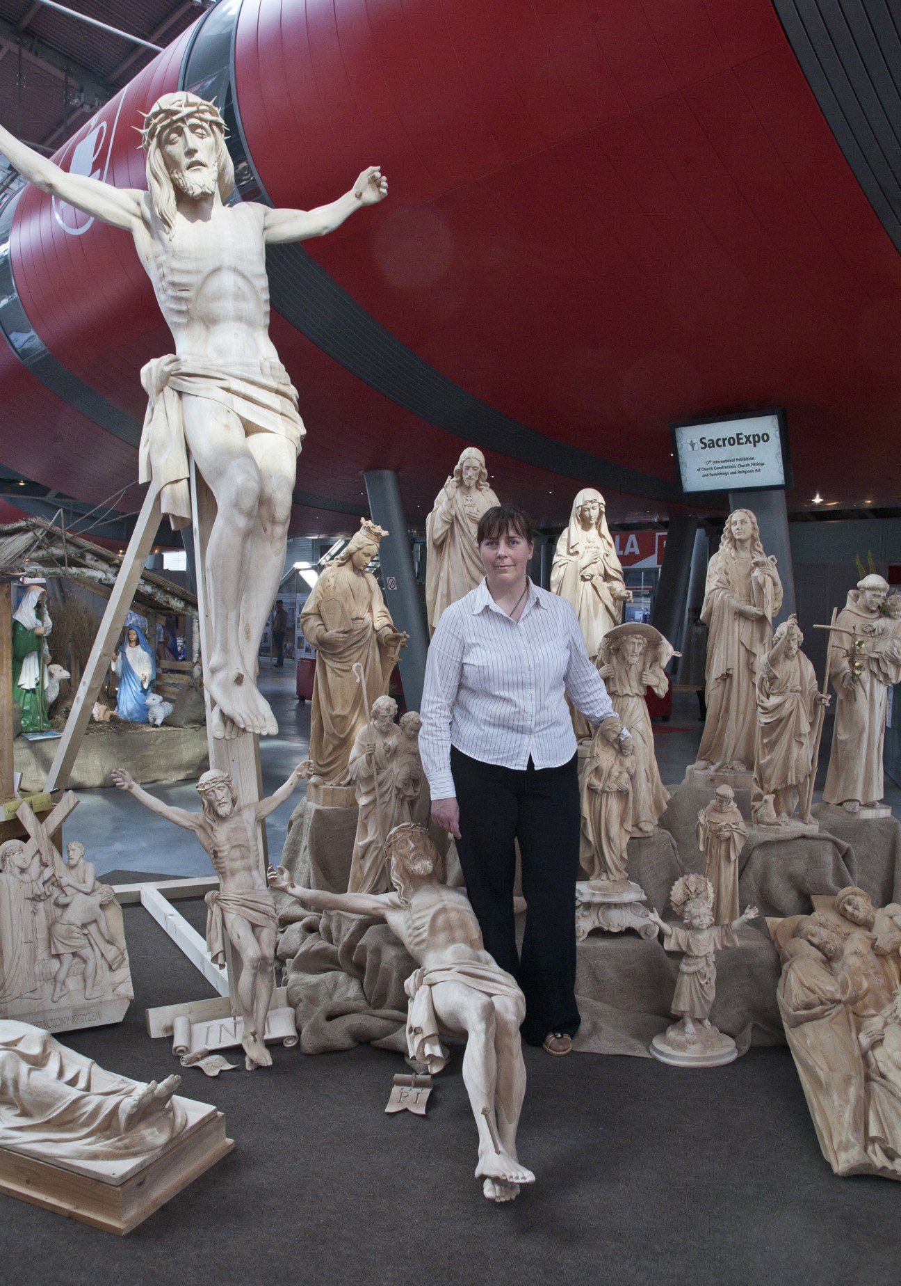 Woman standing among wooden religious statues including a large crucifix at SacroExpo trade fair.
