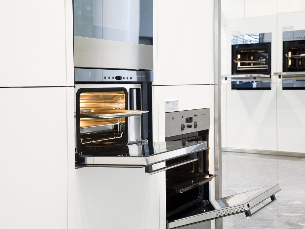 V-Zug built-in ovens displayed in a showroom with white cabinetry and stainless steel appliances.