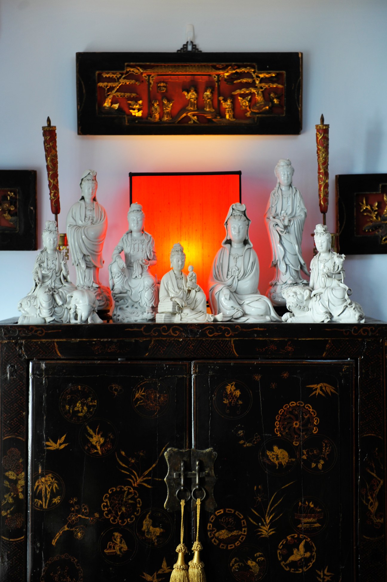 Collection of white ceramic statuettes displayed on a black lacquered cabinet with red illuminated backdrop.