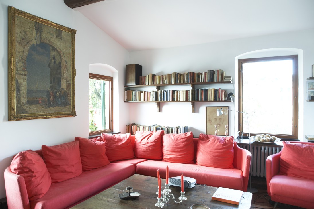 Modern living room with red sofa, bookshelves, and classical artwork at Villa Rosmarino.
