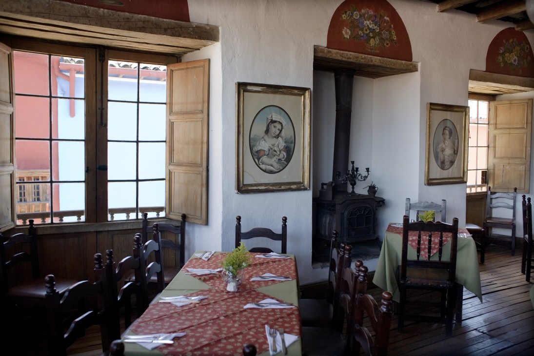 Interior of Fulanitos restaurant with wooden dining tables, colonial furnishings, portraits, fireplace and large windows.