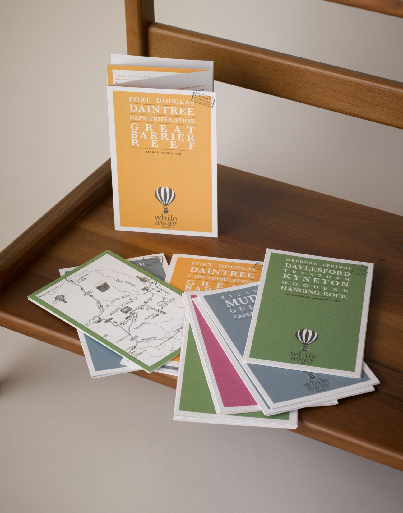 Whileaway travel guides displayed on wooden shelf, showing colorful pocket-sized Australian regional guides with maps and branded covers.