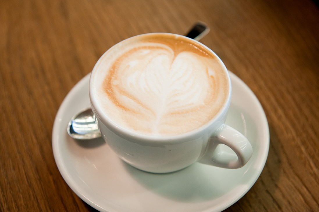 Overhead view of a cappuccino with latte art in a white cup on a wooden table.