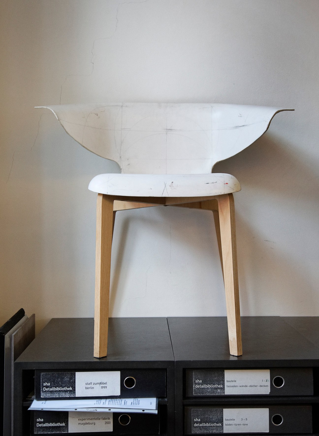 White and natural wood prototype chair with curved backrest displayed on black storage unit.