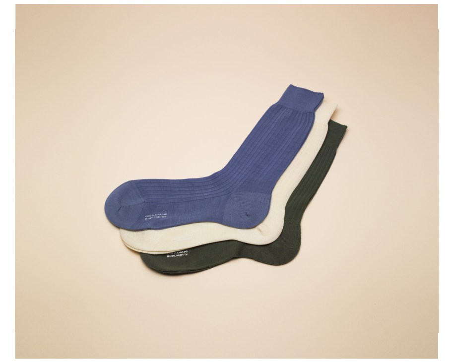 Three luxury socks in blue, cream, and dark green displayed on a beige background.