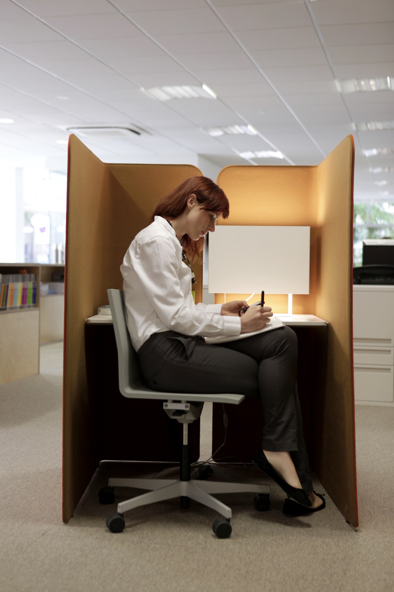 Jana Thoron, London office manager, sits in a modern wooden pod desk working at an office.