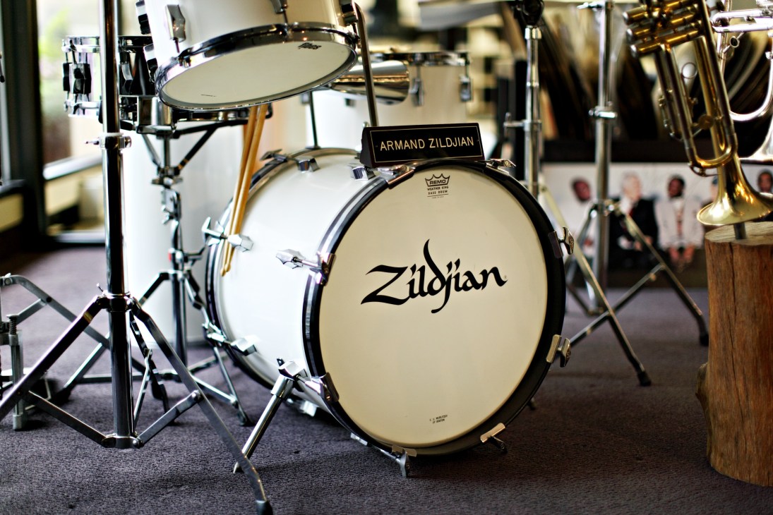 Former CEO Armand Zildjian's drum kit featuring a Zildjian bass drum with cymbals and brass instruments in the background.