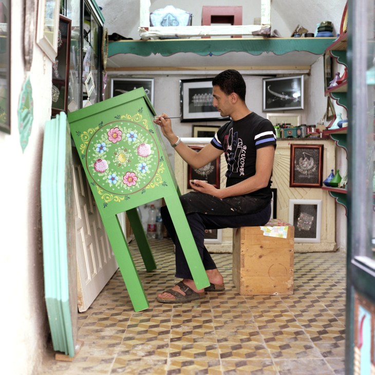 Farid Smaallah painting a green decorative dowry box in his casbah workshop.