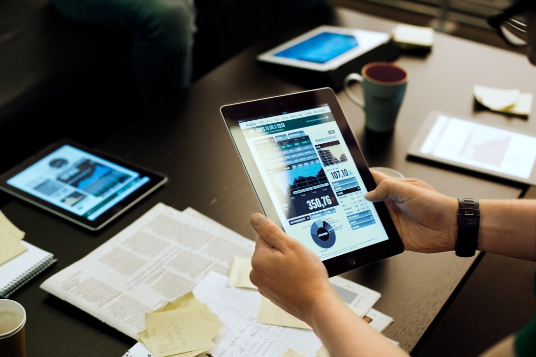 Person holding an iPad displaying the Dagens Næringsliv digital edition with financial data and charts on screen.