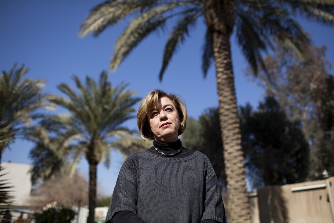 Iraqi MP Mayasoun Damlouji stands outdoors under palm trees wearing a dark sweater.
