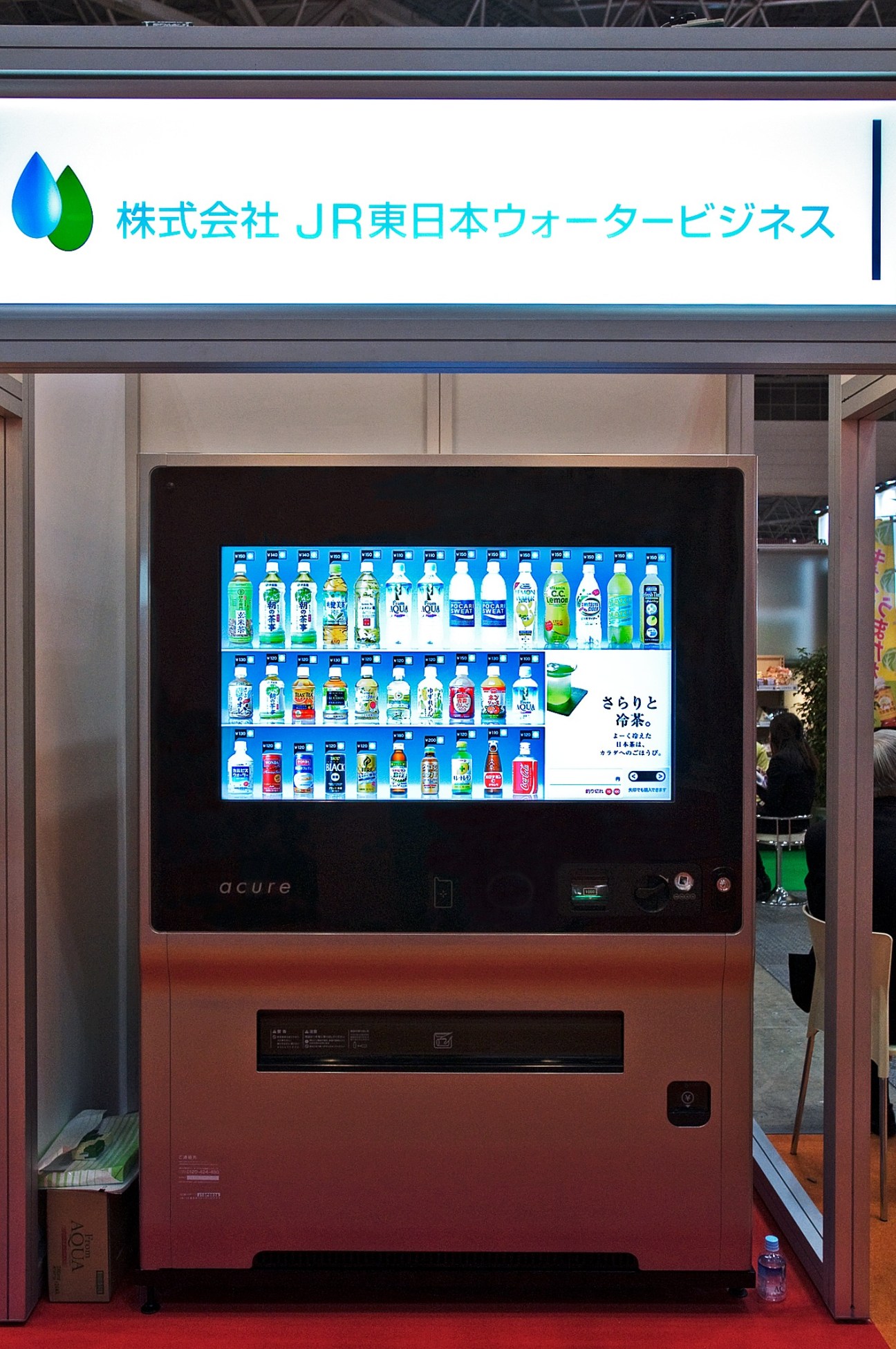 JR East Water Business's red intelligent vending machine displaying beverages on a touchscreen with Japanese signage above.