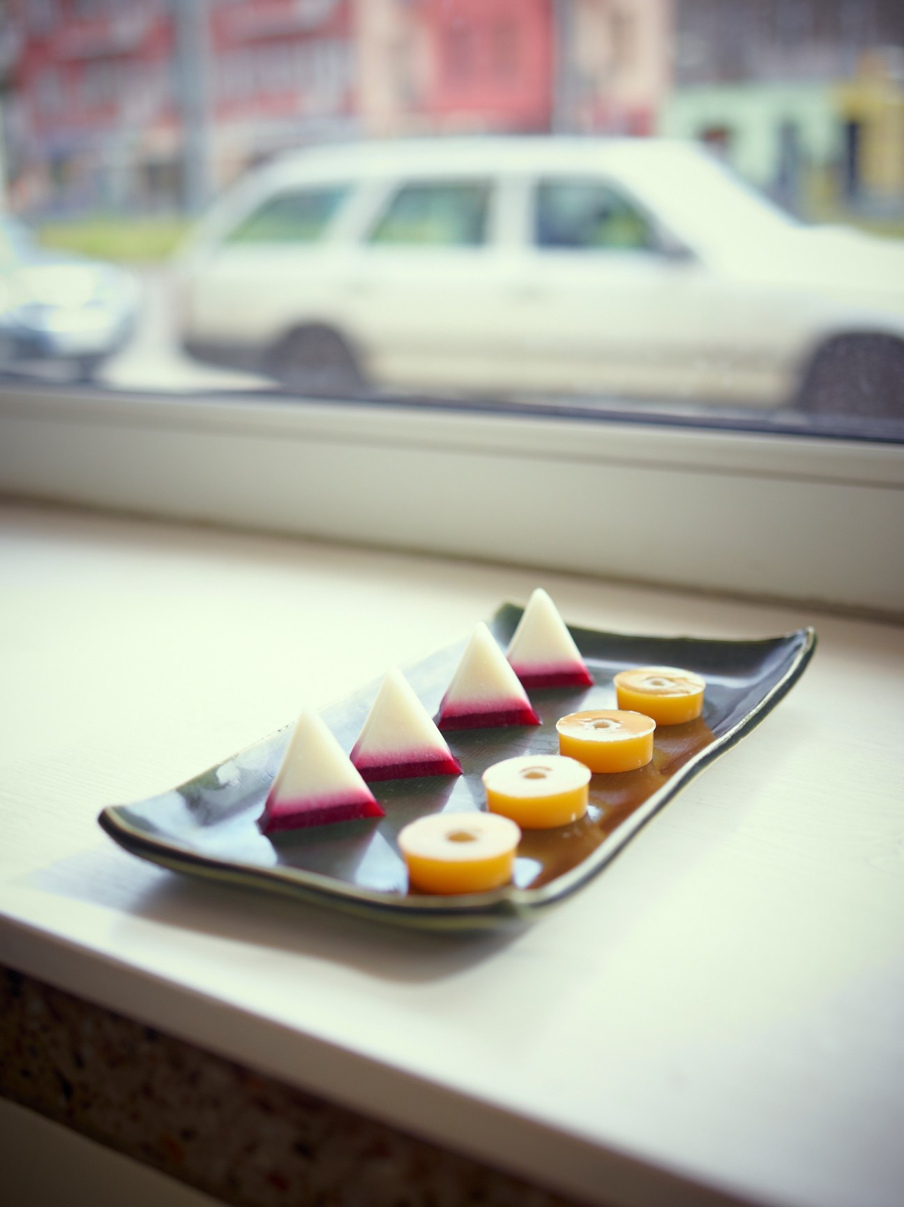 Plated desserts on a dark plate by a window with a blurred white car in the background.