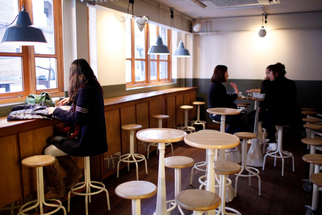 Coffee Kitchen interior with customers at wooden tables and bar seating under pendant lights