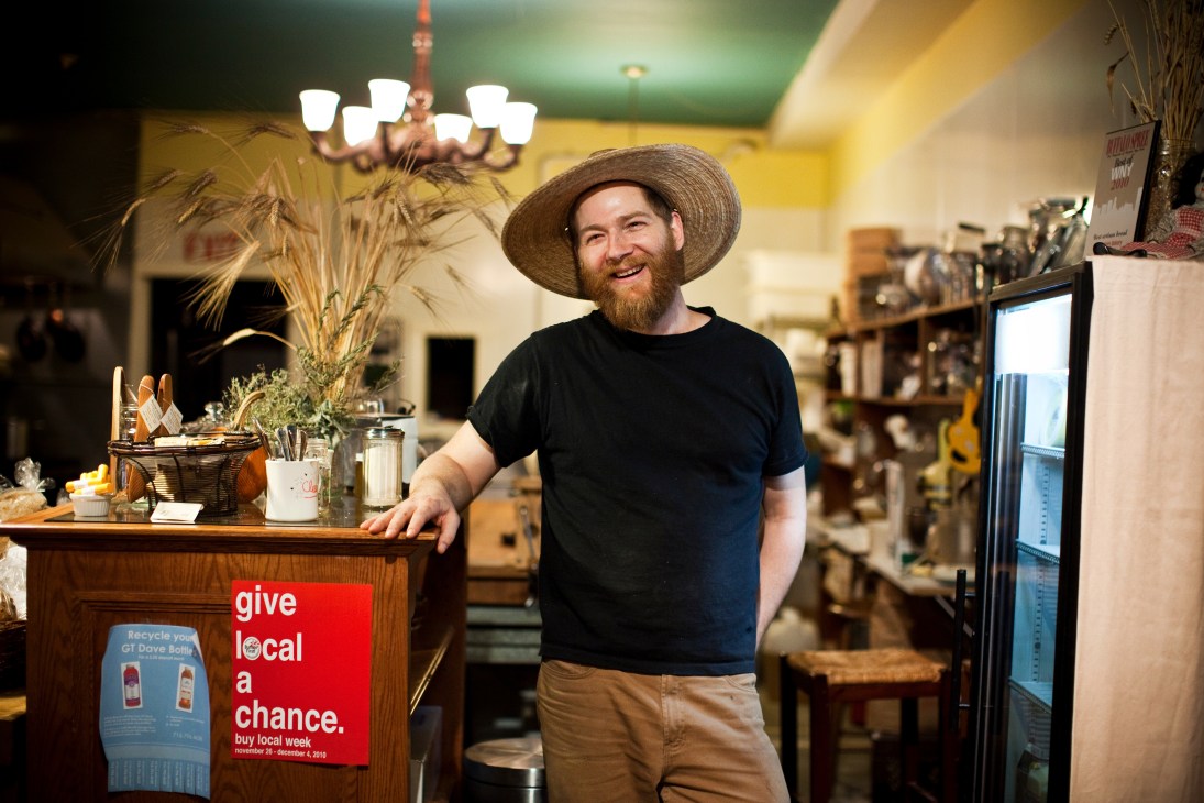 Kevin Gardner stands behind the counter at Five Points Bakery in Buffalo, wearing a straw hat and black shirt.