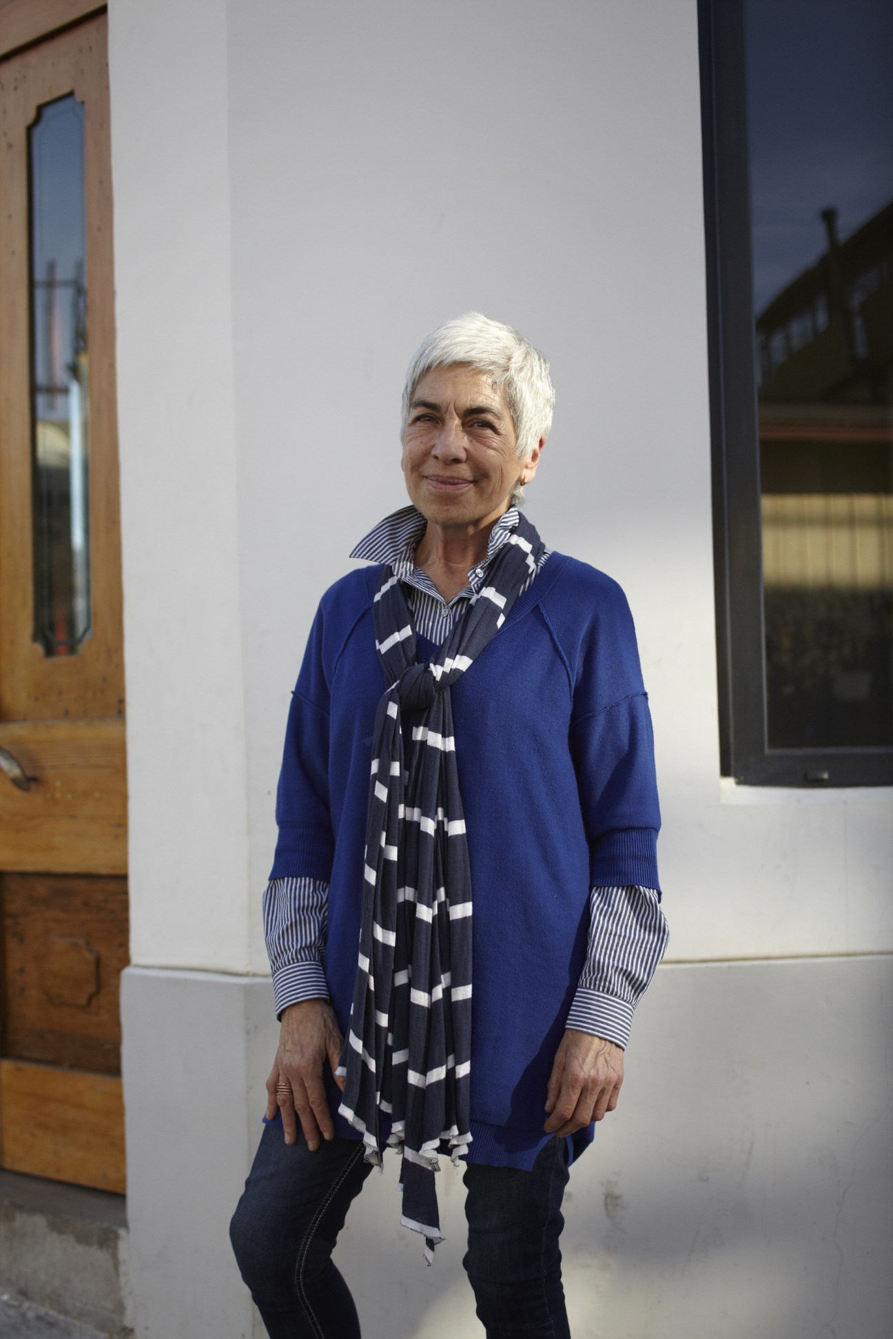 Laura Moreno stands in a modern gallery space wearing a blue cardigan and patterned scarf.