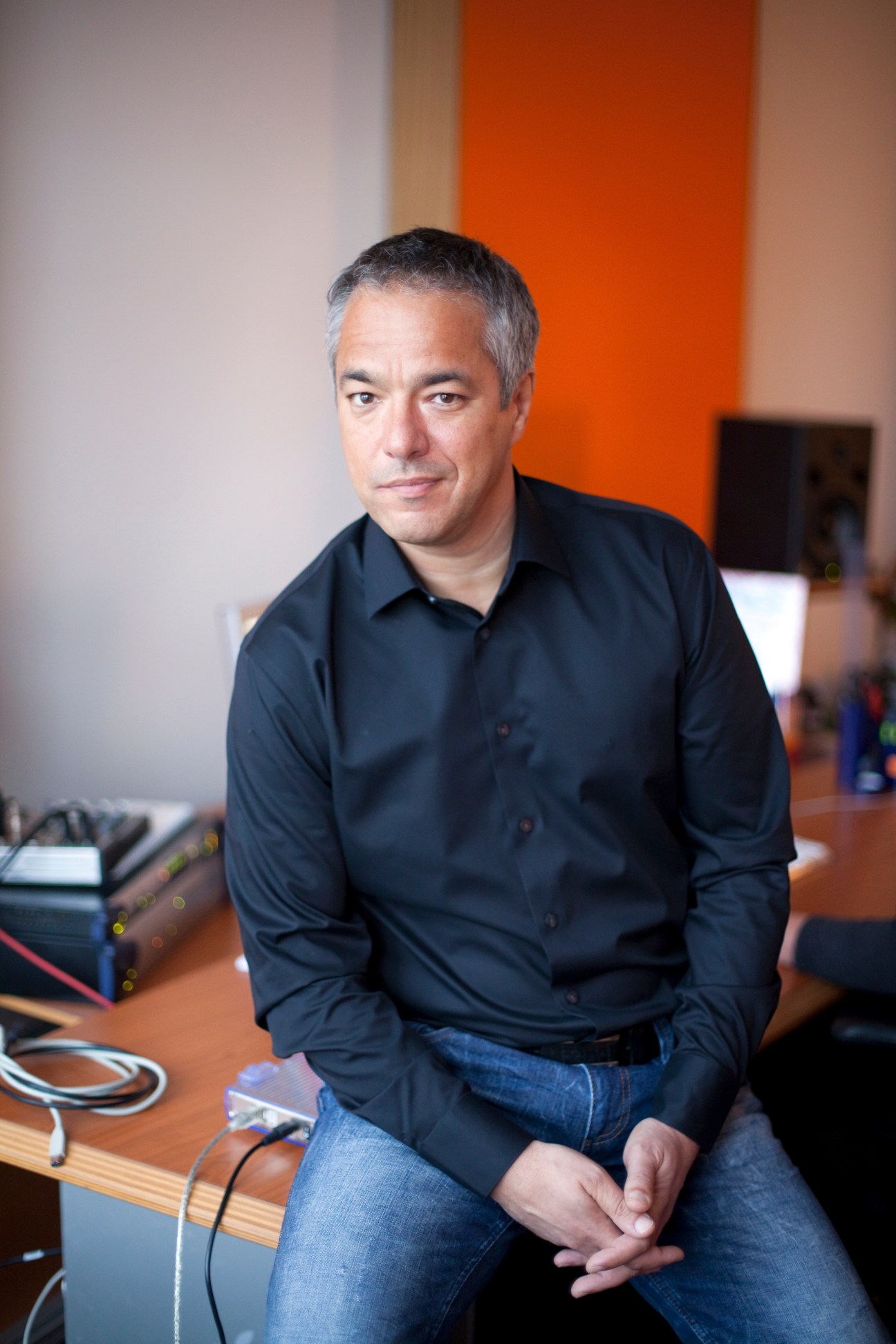 Charles Rettinghaus, German voice actor, sitting at a desk in a studio with an orange wall behind him.
