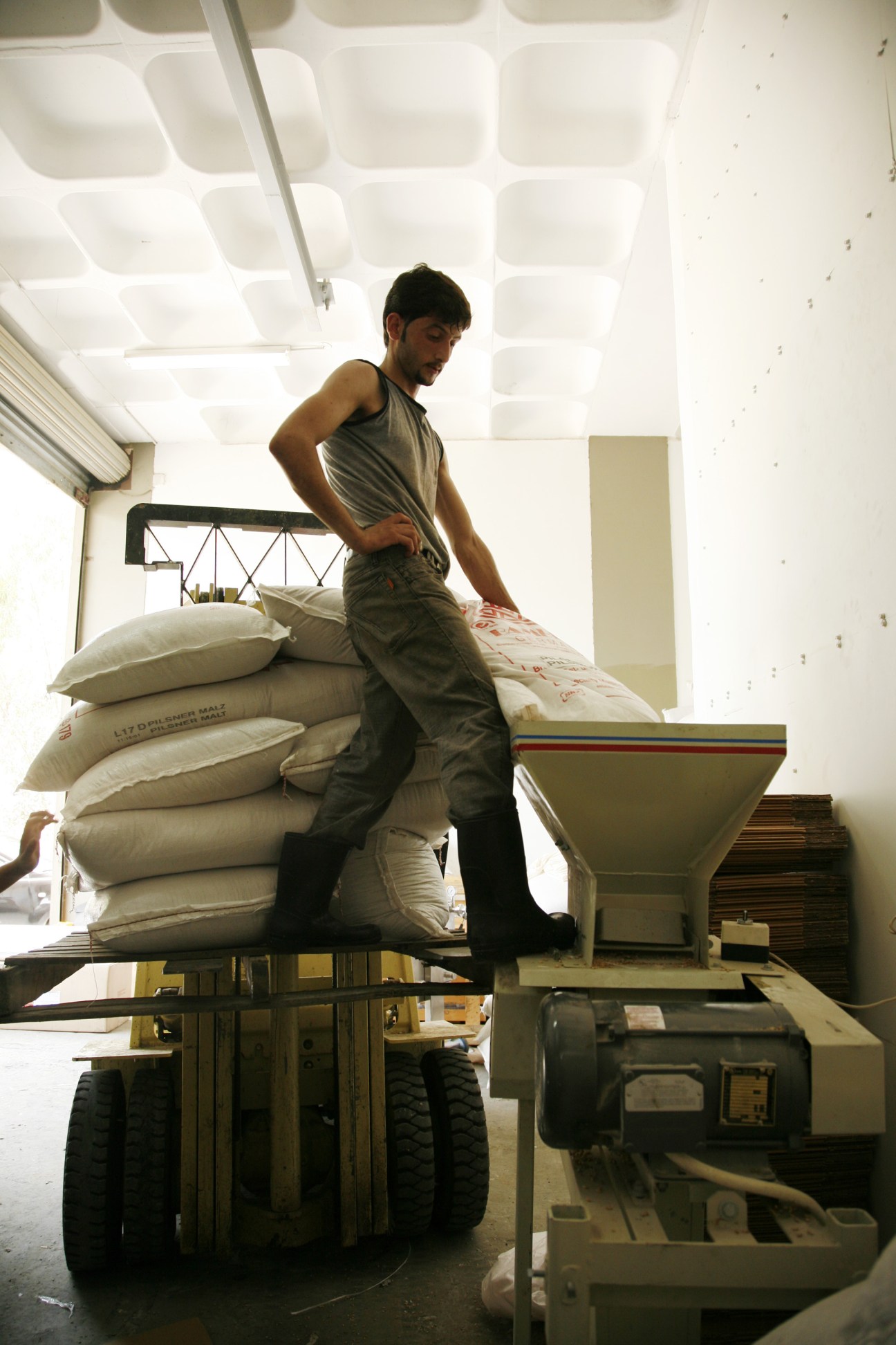 Man standing on forklift with stacked grain sacks at LB beer brewery facility.
