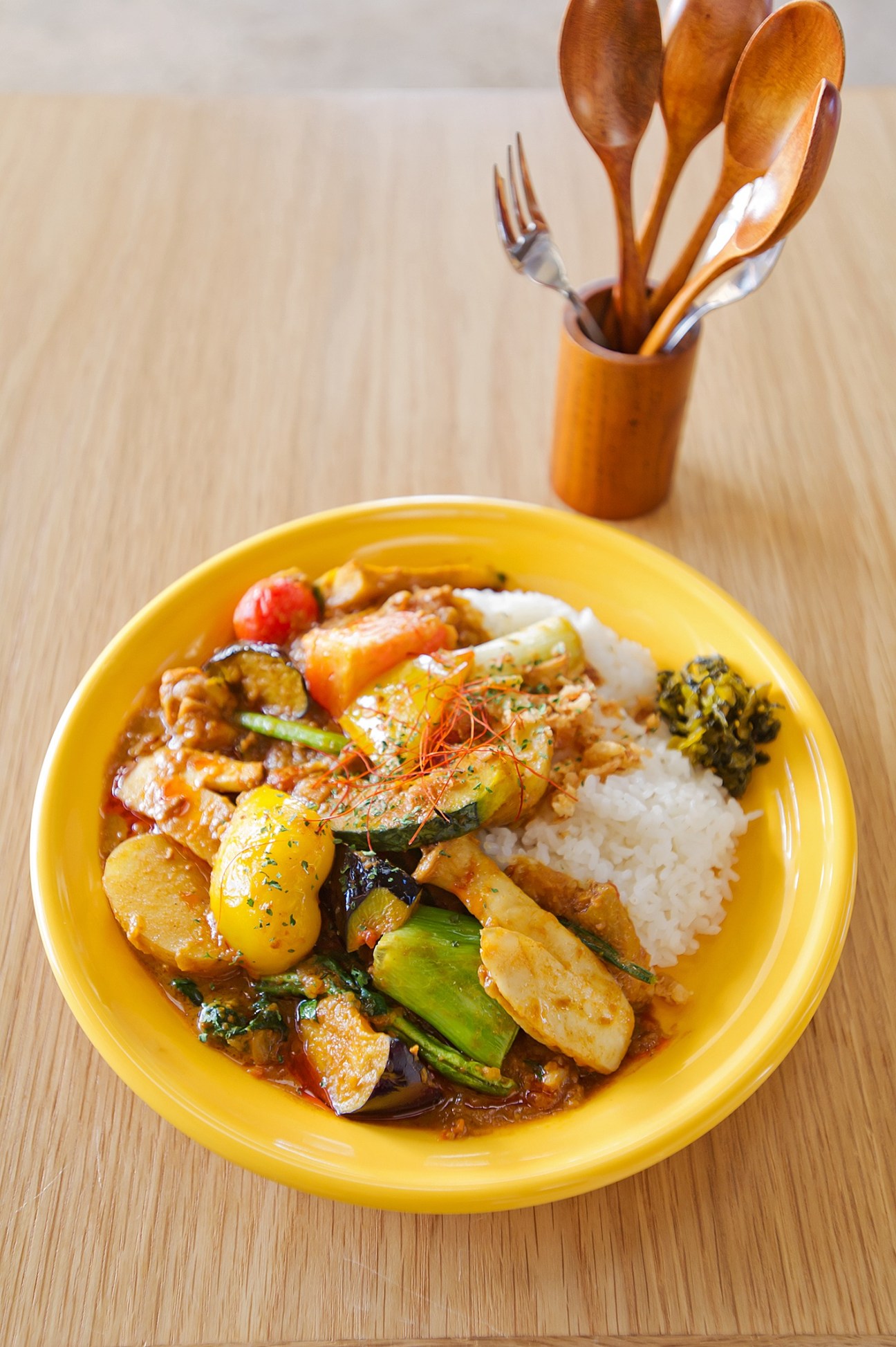 Yellow bowl of stir-fried shrimp and vegetables with rice on wooden table.