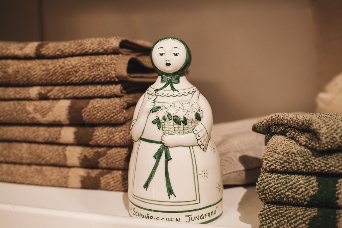 Porcelain doll figurine with green accents surrounded by folded loden wool textiles.