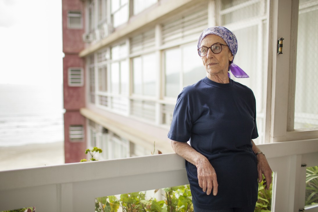 Valkiria Ortega Donoso, an 80-year-old resident, stands by a window in her Parque Verde Mar apartment overlooking the building's facade.